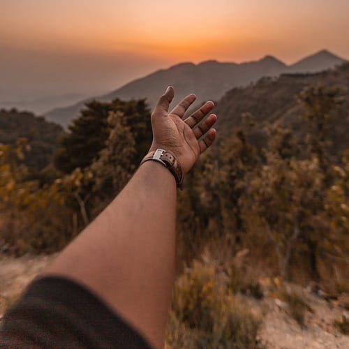 man reaching his hand in the direction on mountains at sunset