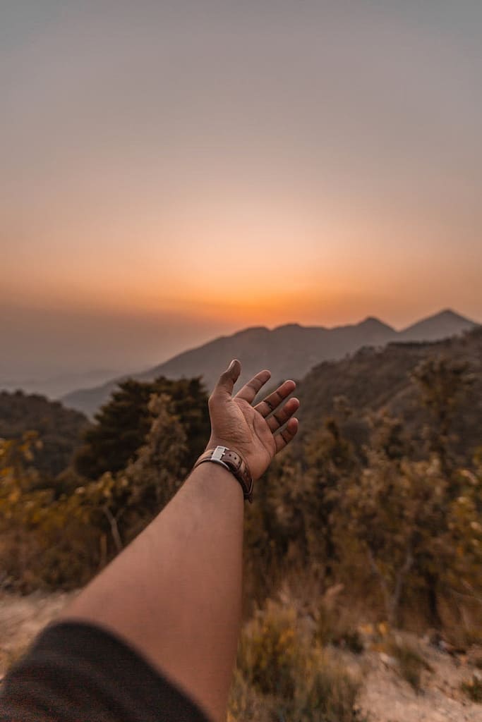 man reaching his hand in the direction on mountains at sunset