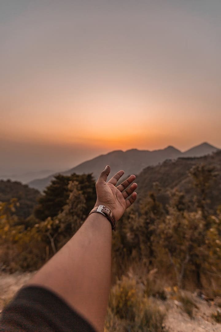 man reaching his hand in the direction on mountains at sunset