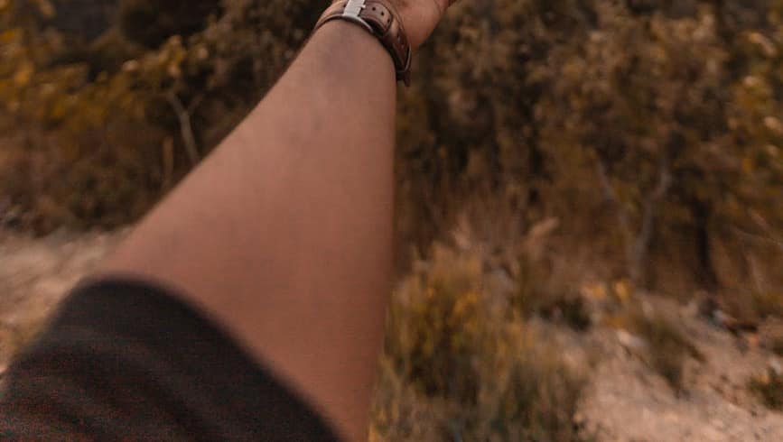 man reaching his hand in the direction on mountains at sunset